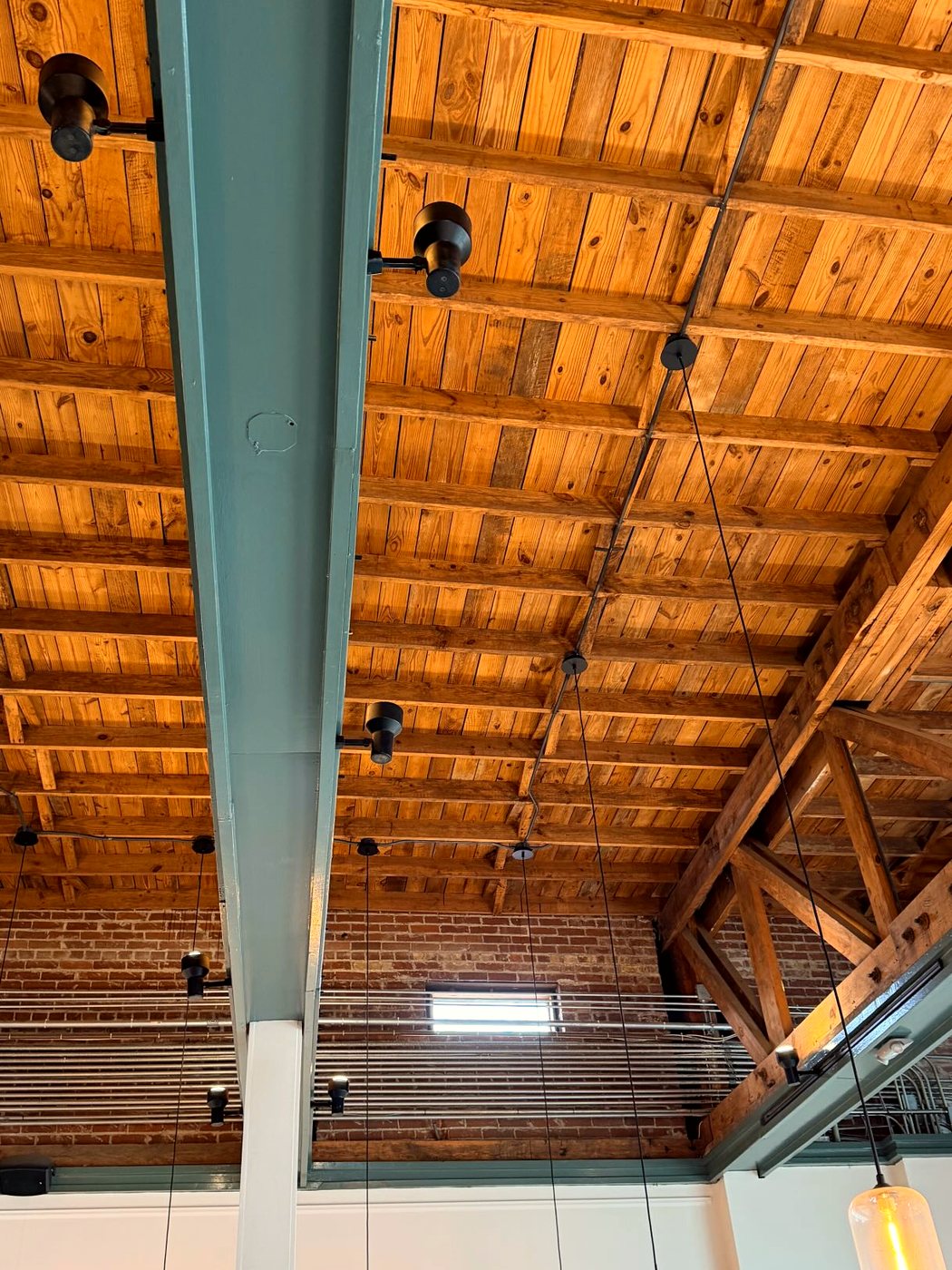 The timber roof trusses and a teal steel column overhead