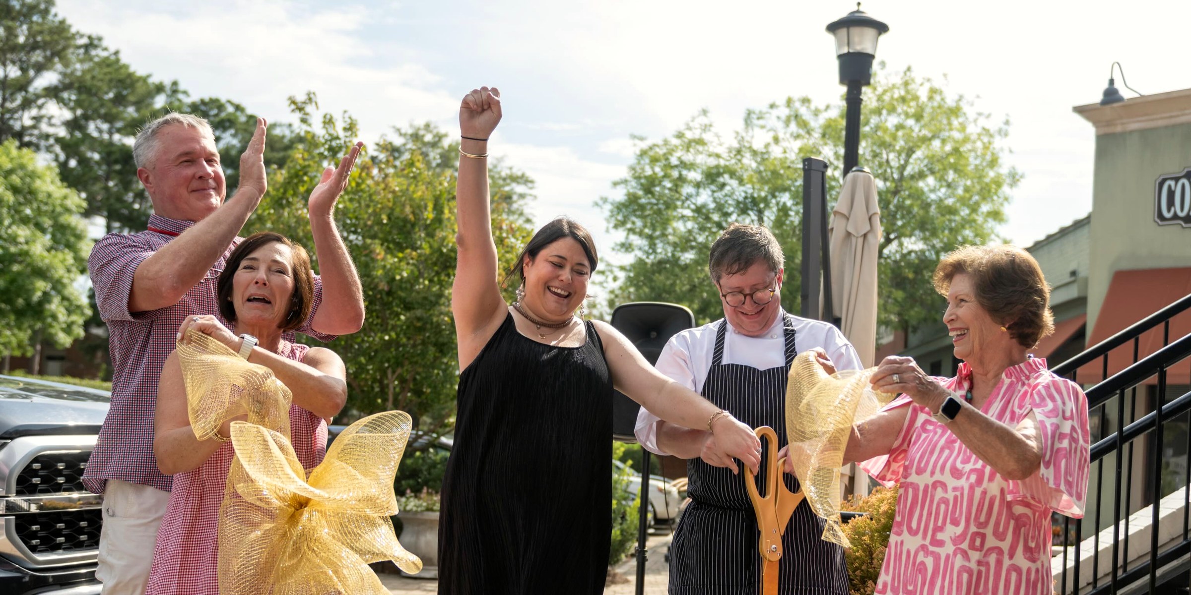 The ribbon cutting outside Lou Lou's and Foster's on 13th Street, gold scissors and the whole street watching