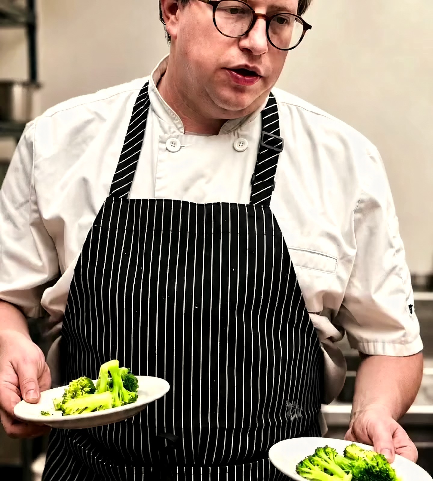 Chef Scott Ailsworth at the pass in his whites and striped apron, plating two dishes