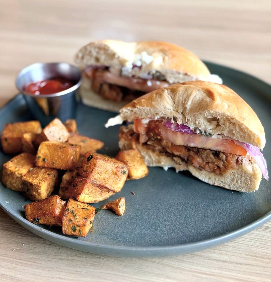 A fried sandwich with tomato and red onion, and a side of seasoned potatoes
